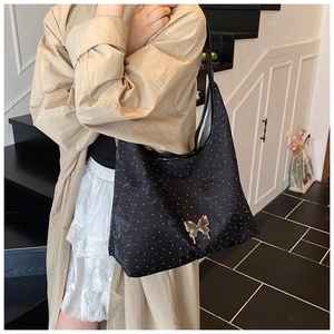 Détail d'un sac cabas noir avec papillon en métal argenté et motifs à pois blancs