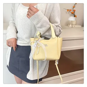 Detail of yellow lychee grain leather bucket bag with lace bow and pearl charm