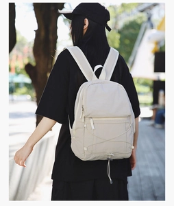 Detail view of beige nylon backpack featuring front elastic bungee cord system on model