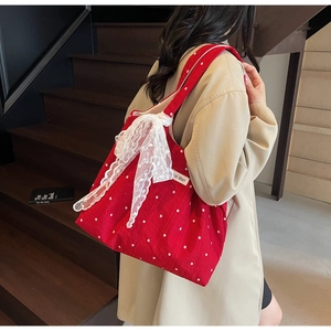 Détail du sac cabas en toile rouge à fleurs avec un élégant nœud en dentelle blanche sur le côté