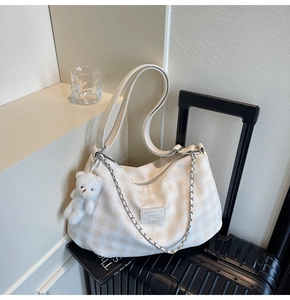 Detail of checkered tote bag with plush bear charm and silver chain on luggage