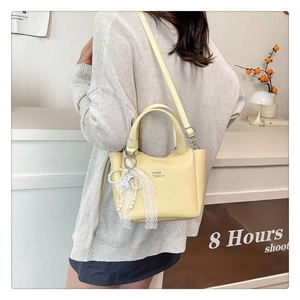 Close-up of a yellow pebbled leather bucket bag with lace bow and pearl charm detail