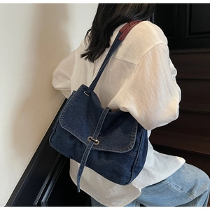 Detail of vintage denim shoulder bag with leather strap and metal clasp on female model