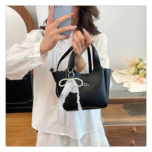 Detail of black faux lizard skin bucket bag featuring pearl lace bow and metal logo