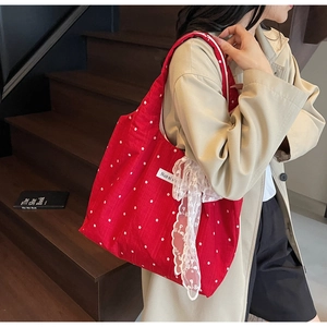 Détail du sac cabas rouge à fleurs avec un grand nœud en dentelle blanche sur le côté