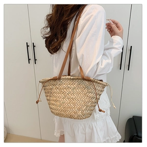 Détail du sac seau en paille tressée avec bandoulière en cuir brun et cordon