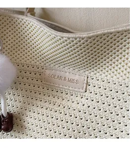 Détail du sac en maille avec étiquette de marque et charm décoratif à pompon doux