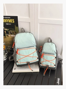 Detail view of mint green and grey waterproof nylon backpacks with orange bungee cords