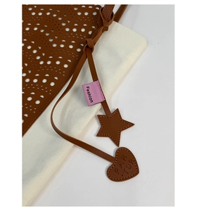 Close-up of brown leather tote bag with laser-cut patterns and star shaped charms