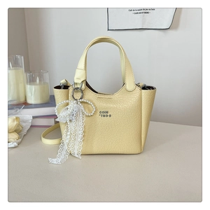 Detail of yellow embossed leather bucket bag with lace bow and pearl charm accessory