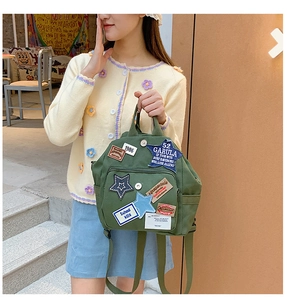 Detail eines grünen Canvas-Rucksacks mit Vintage-Patches und Griffen am Modell gezeigt