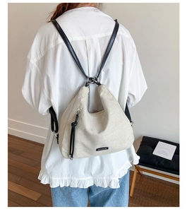 Detail view of large beige canvas hobo bag with black leather straps on a model