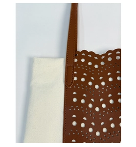Detail of canvas tote with laser-cut brown leather pattern and fine stitching