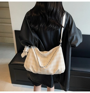 Detail view of cream checkered crossbody bag with chain and plush bear charm