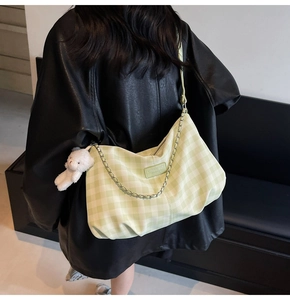 Close-up of green plaid shoulder bag with metal chain and plush bear charm detail