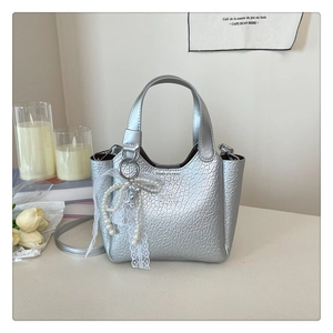 Detailed close-up of silver metallic bucket bag with pearl lace charm and crossbody strap