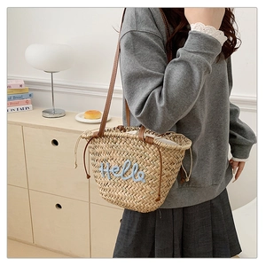 Détail du sac cabas en paille tressée avec broderie Hello bleue et bandoulière en cuir