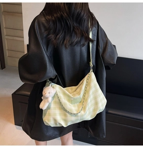 Detail of light green plaid shoulder bag with plush bear charm and metallic chain link