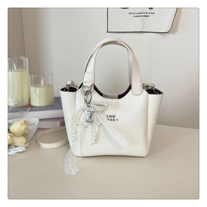 Detail of cream bucket bag with crocodile texture, pearl lace charms and cartoon pendant