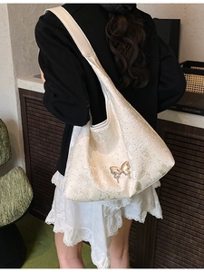 Sac hobo blanc crème avec pendentif papillon argenté porté à l'épaule pour femme