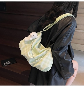 Detail of green checkered tote bag with plush bear charm and metallic chain accent