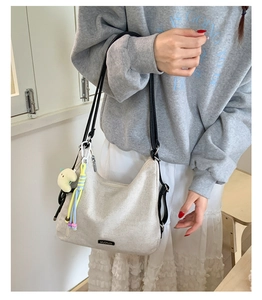 Detail of canvas underarm bag with black brand label and colorful tassel doll accessory