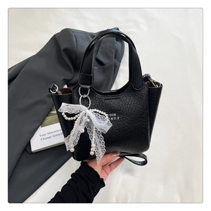 Detail of black ripple textured leather bag with lace bow and pearl charm accents