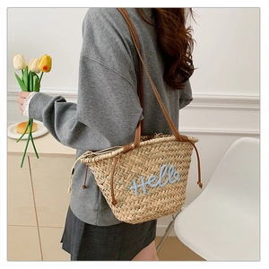 Détail du sac fourre-tout en paille avec broderie Hello et anses en cuir marron