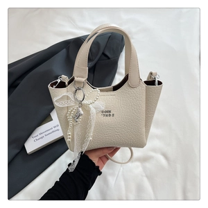 Detail of cream bucket bag with crinkled texture, pearl lace bow, and metal bear charm