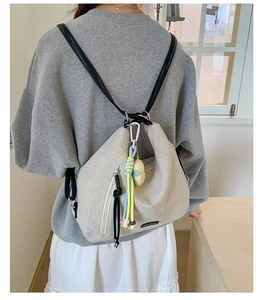 Detail of cream canvas backpack with contrast leather straps and woven pendant accessory