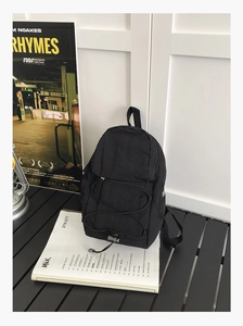 Detail of a black mini nylon backpack showing front zipper pocket and elastic drawstring