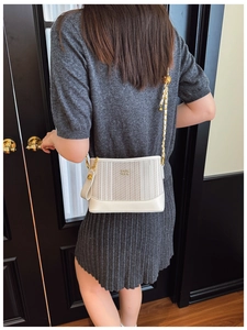 Détail d'un sac à bandoulière rayé blanc avec chaîne dorée et boule métallique