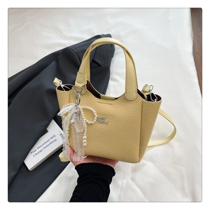 Detail of yellow crocodile embossed bucket bag with pearl lace bow and metal lettering