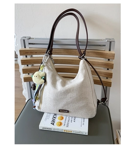 Detail of beige canvas tote with brown leather straps and plush cartoon pendant charm