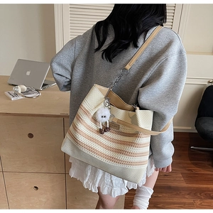 Détail d'un grand sac cabas en maille avec lanières en cuir marron et pompon en peluche blanc