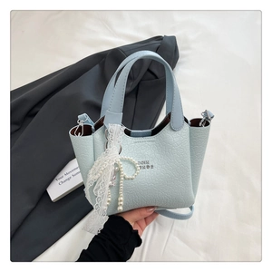 Detail of light blue bucket bag with lace ribbon and pearl bow charm on gray blazer