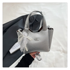 Detail of silver metallic bucket bag with pearl lace bow and textured leather surface