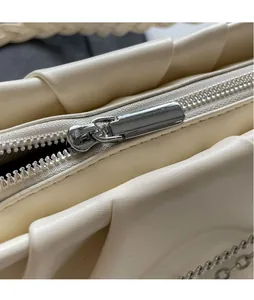 Gros plan d'un sac en cuir plissé crème avec fermeture éclair argentée et chaîne décorative