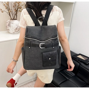 Deep grey canvas backpack with silver buckles shown on a model in a minimal interior