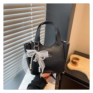 Detail of black textured bucket bag with lace bow and pearl charm against soft lighting