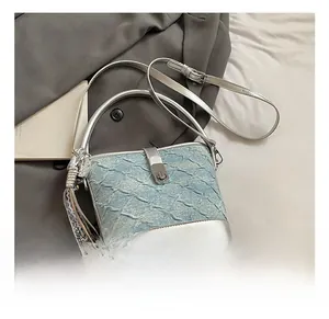 Dettaglio della borsa a secchiello blu chiaro con finiture in pelle argento sul letto
