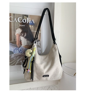 Close-up of cream canvas tote bag with black strap, logo plate, and cute moon charm