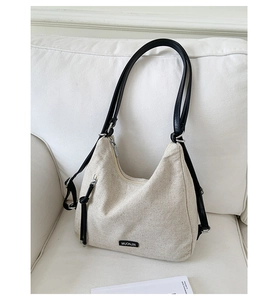 Detail of off-white canvas tote bag with black leather strap and brand plaque