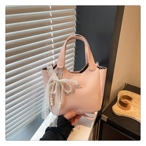 Detail of light pink crocodile pattern bucket bag with pearl lace bow charm