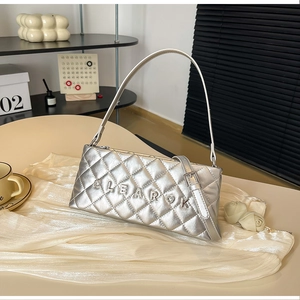 Detail of silver quilted handbag with metal letter logo on a minimalist table
