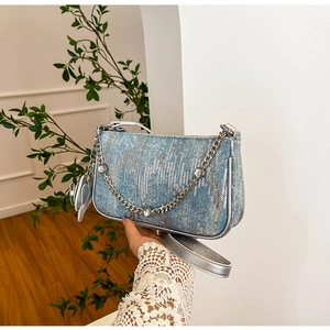 Detail of blue denim shoulder bag with silver sequins and heart-shaped pendant charm