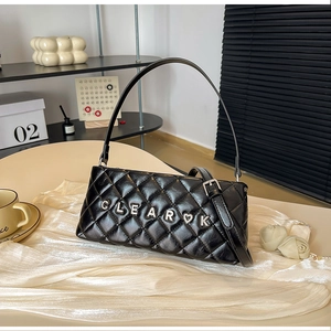 Detail shot of black quilted shoulder bag with silver metal letter buckle on beige table