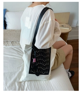 Detail of canvas tote bag with black laser-cut patterns and decorative charms on a model