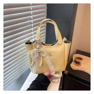 Detail of pale yellow crocodile texture bucket bag with lace bow and pearl tassel