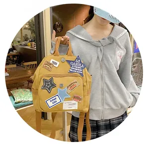 Detail eines senfgelben Canvas-Rucksacks mit Vintage-Buchstaben-Patches und Stickerei-Motiv